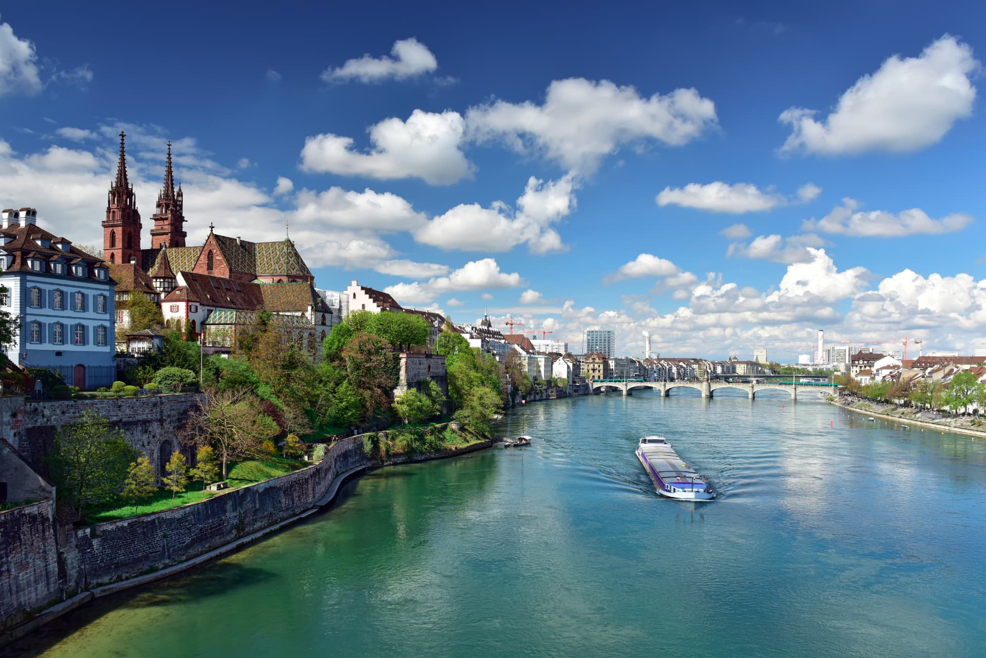Der Rhein in Basel in der Schweiz, mit dem Basler Münster und einer Frachtbarke auf dem Wasser