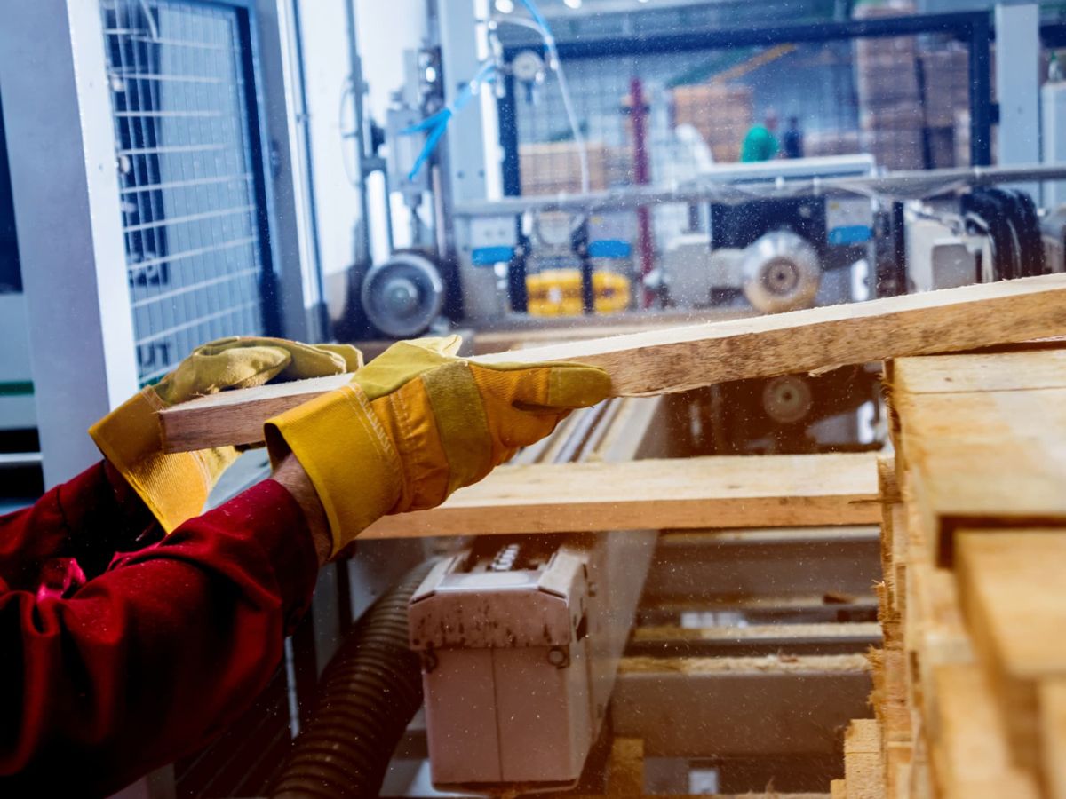 Mani con guanti che maneggiano tavole di legno segato in uno stabilimento